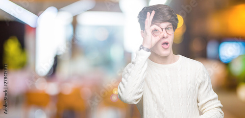 Obraz na plátně Young handsome man wearing glasses over isolated background doing ok gesture shocked with surprised face, eye looking through fingers