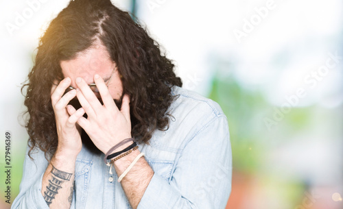 Young hipster man with long hair and beard wearing glasses with sad expression covering face with hands while crying. Depression concept. © Krakenimages.com