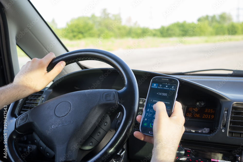 A man dials a phone number on touch screen of smartphone while driving a car