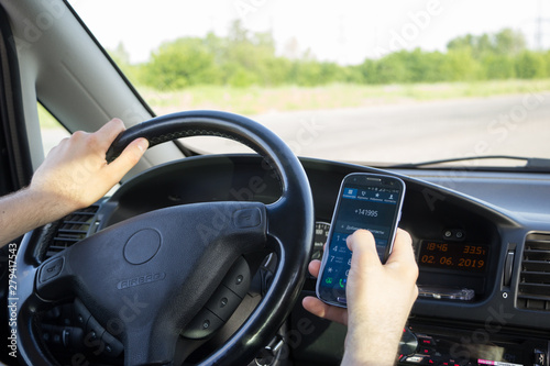 A man dials a phone number on touch screen of smartphone while driving a car