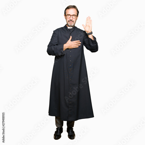 Middle age priest man wearing catholic robe Swearing with hand on chest and open palm, making a loyalty promise oath