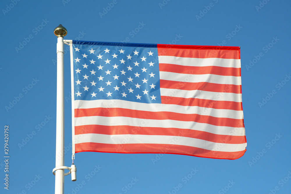 USA  flag flapping against blue sky without clouds. American flag waving in the wind on flagpole on sunny day. Patriotic symbol of the United States of America.