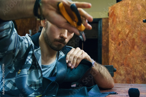 Young man sews leather goods. Craftsman creates leather object. Making handmade item. Guy working with needle pliers. Male hands with needle and thread