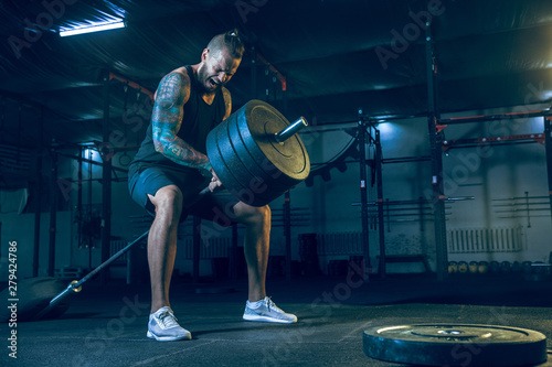 Fototapeta Naklejka Na Ścianę i Meble -  Young healthy man athlete doing exercise with the barbell in the gym. Single male model training hard and practicing in lunges. Concept of healthy lifestyle, sport, fitness, bodybuilding, crossfit.