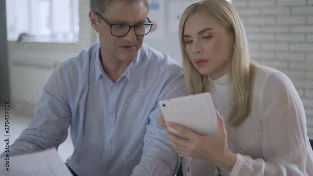 Businessman looking at financial graphs and charts in a tablet. Business meeting. Coworkers talking in the background. 4K Businessman looking at financial graphs and charts in a tablet. Business meeting. Coworkers talking in the background. 4K