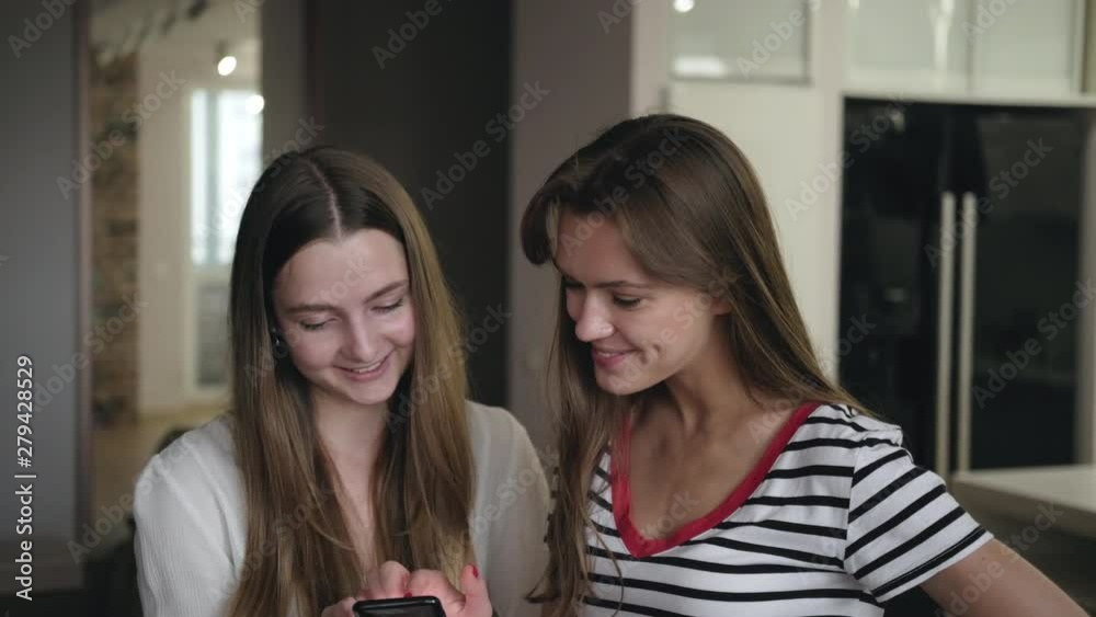 two young women are standing in the room and reading messages on the phone. Close up portraits two young women are standing in the room and reading messages on the phone. Close up portraits