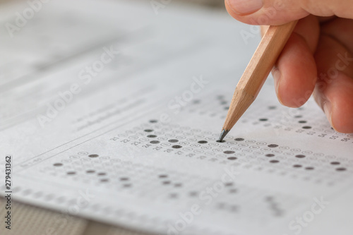 Student hand testing doing test exam with pencil drawing selected choices on answer sheet in school final exams at college or university. Taking multiple choice for assessment in examination classroom photo