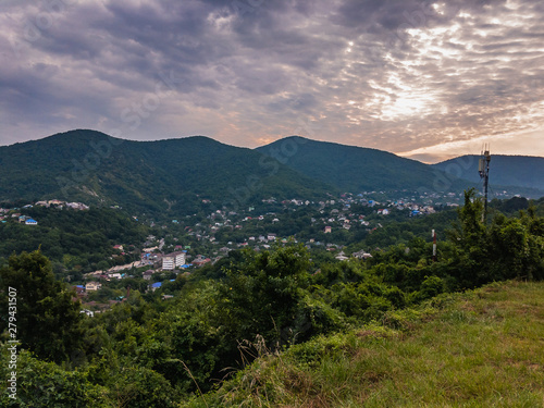 Small town between high mountains covered with green plants under a blue cloudy sky on a summer morning. © Vit-Vit