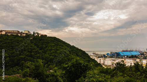 View of the mountain covered with green trees and city buildings under the mountain on a summer sunny day.