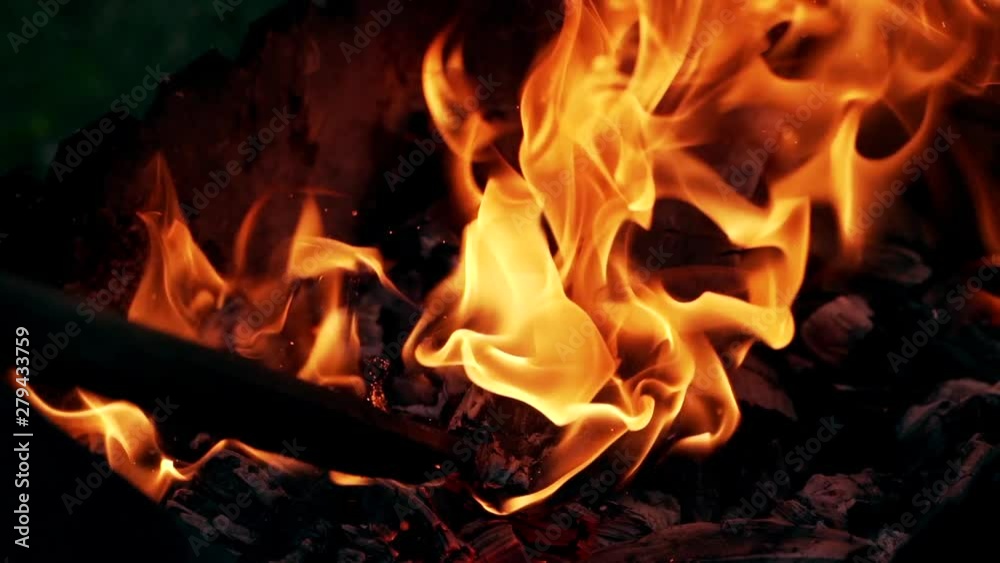 Bright fire motion. Sparkles of red and yellow flame from smoldered logs. Wooden stick beats a black log in the burning fire. Slow motion.