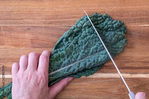 Woman slicing a bunch of dark green, crinkly, Lacinato Kale leaves, on a wood cutting board, hands and chefs knife photo