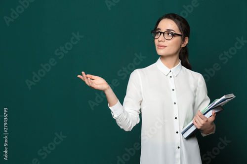Portrait of beautiful young teacher with books near chalkboard, space for text
