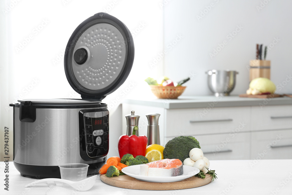 Modern multi cooker and products on table in kitchen. Space for text