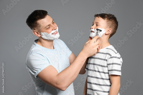 Photos Dad pretending to shave his son with razor on grey background