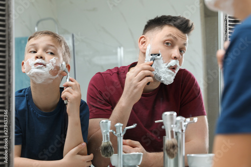 Dad shaving and son imitating him at mirror in bathroom