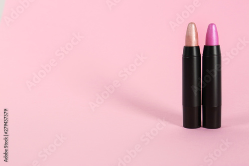 Bright lipsticks in black tubes on pink background, space for text