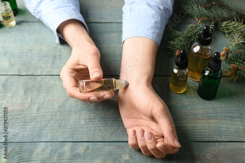 Woman applying essential oil on wrist at wooden table, closeup