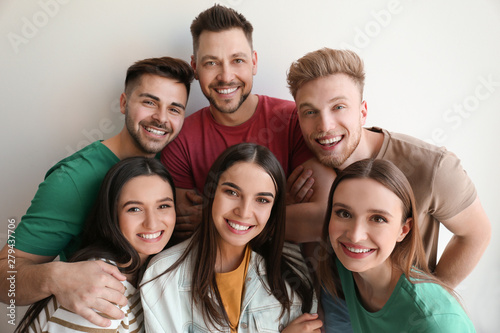 Group of happy people posing near light wall