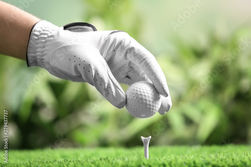 Player putting golf ball on tee against blurred background, closeup
