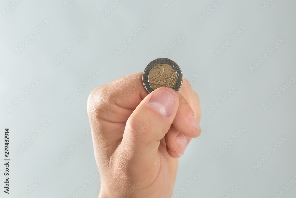 Young man holding coin on grey background, closeup Young man holding coin on grey background, closeup