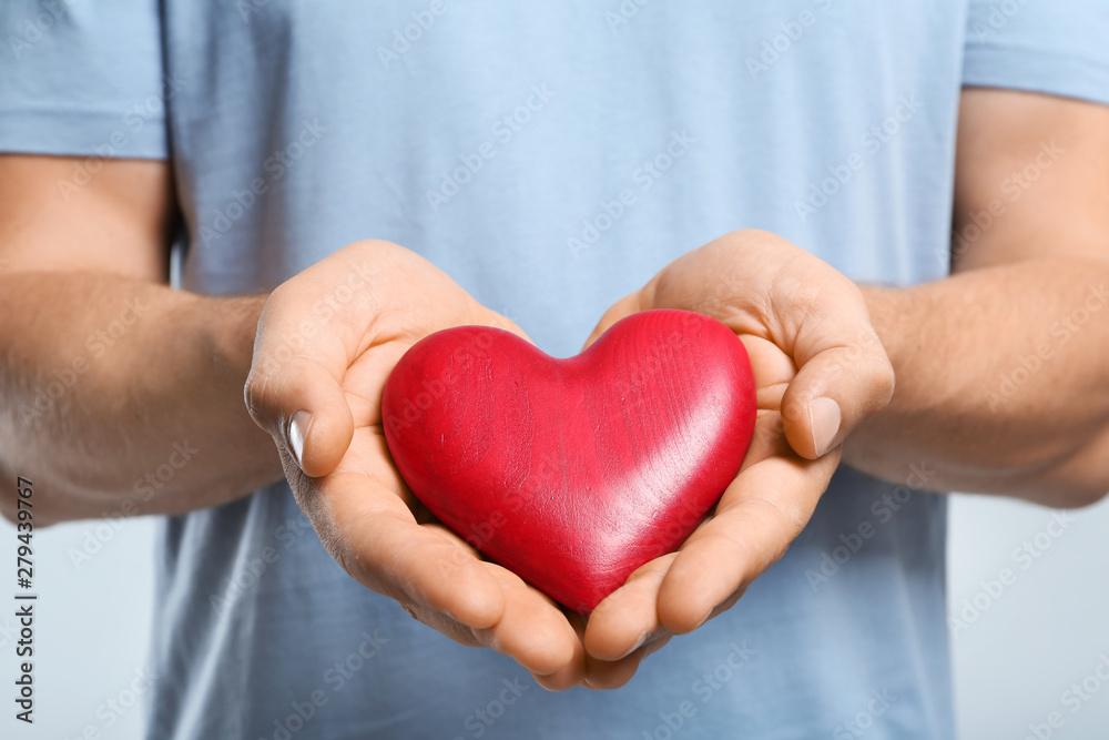 Young man holding red heart on color background, closeup. Donation concept