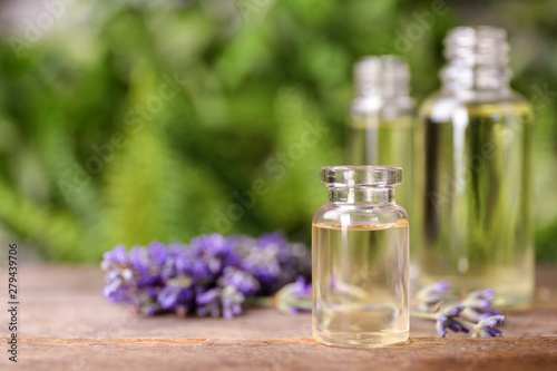 Bottles with natural lavender essential oil on wooden table against blurred background. Space for text