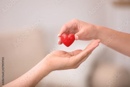 Fényképezés Woman giving red heart to man on blurred background, closeup