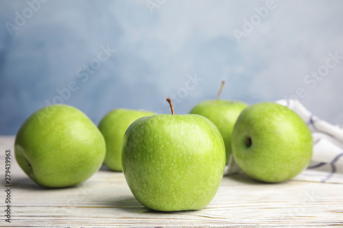 Fresh ripe green apples on white wooden table against blue background, space for text