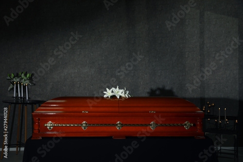 Foto Wooden casket with white lilies and burning candles in funeral home