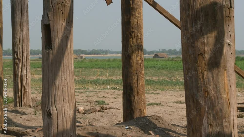 A close up shot of the pillars of a wooden bridge overlooking a field in Myanmar A close up shot of the pillars of a wooden bridge overlooking a field in Myanmar