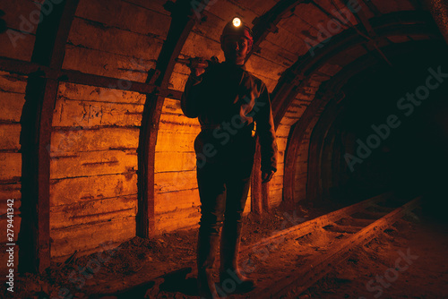 A man in work overalls and a helmet with a jackhammer on his shoulder is standing on the rails. Silhouette in red. Mine worker. Miner © Светлана Наклейщиков