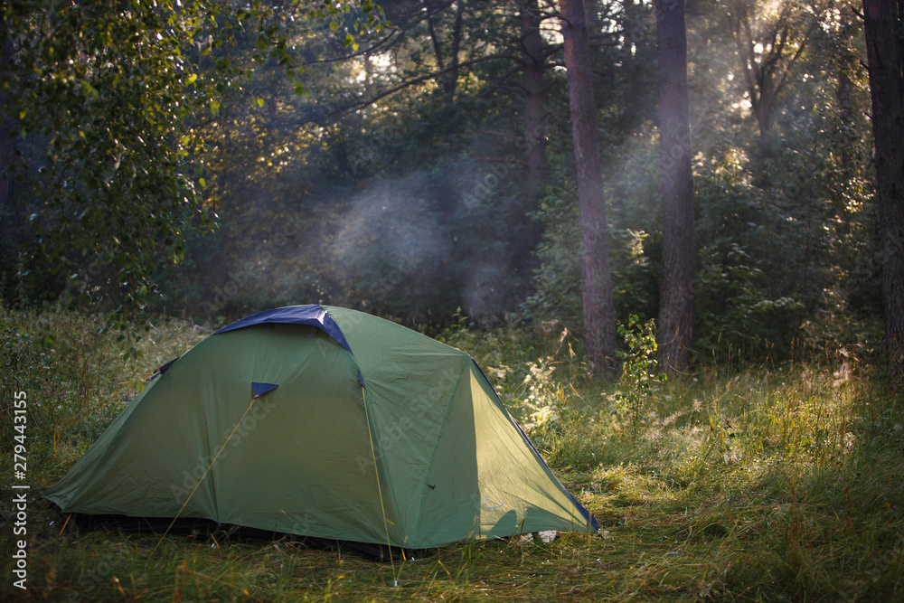 Green tourist tent stands in the woods, illuminated by rays of light. Established tent in the campaign.
