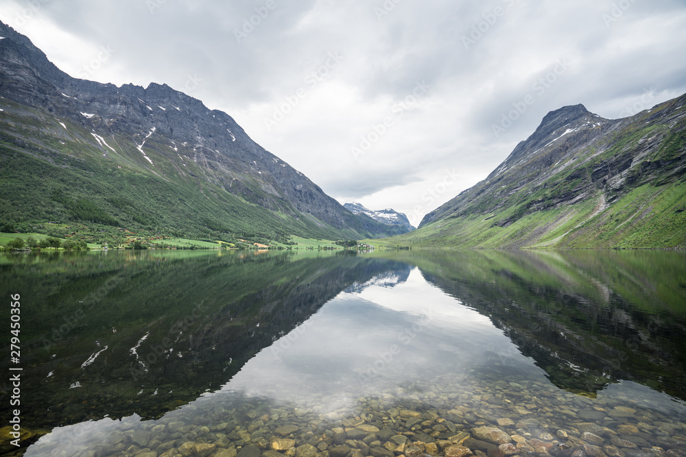 Panorama of beautiful  Overdalen valley. Reflections of the slopes in the mountain lake, symmetrical centered scene. Cloudy summer day in Norway, Scandinavian pearl.