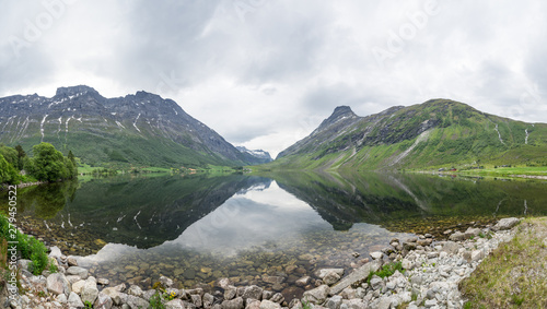 Panorama of beautiful Overdalen valley. Reflections of the slopes in the mountain lake, symmetrical centered scene. Cloudy summer day in Norway, Scandinavian pearl.