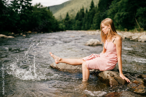 Young happy girl kicking foot in river and splashing water.