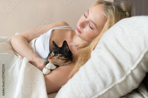 Young beautiful girl sleeping on bed with lovely kitten