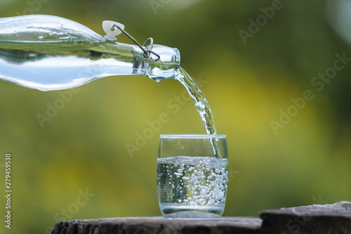 Hand pouring drink water from bottle into glass with natural background © Naypong Studio