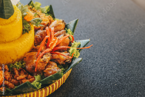 Traditional Indonesian Cuisine Nasi Tumpeng for Celebration. Tumpeng is a cone-shaped rice dish like mountain with meats usually eat as breakfast or lunch isolated on wooden background. photo