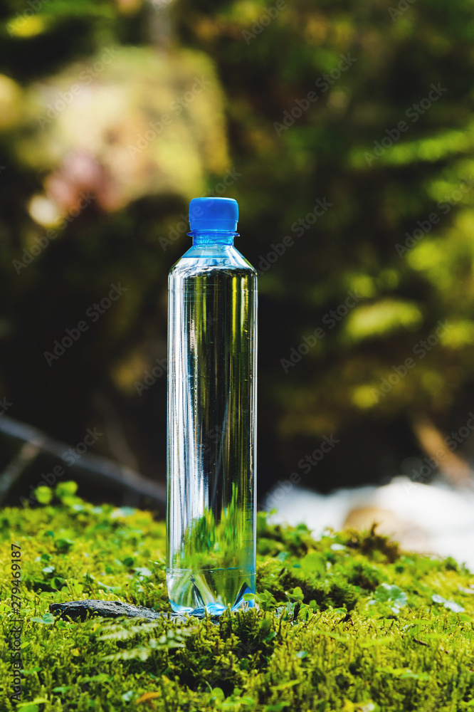 Plastic bottle blue cap with fresh drinking water on a background of green forest stands on a stone with moss. The concept of pure natural mountain water Plastic bottle blue cap with fresh drinking water on a background of green forest stands on a stone with moss. The concept of pure natural mountain water
