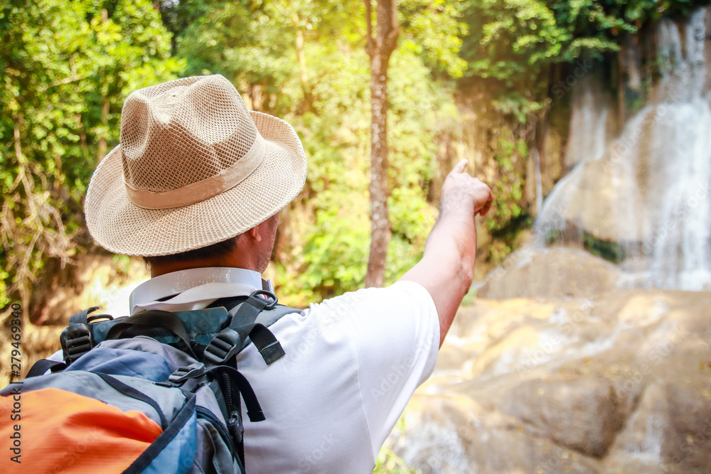 Asian tourists are walking in the forest to see beautiful waterfalls. He wears a hat and backpack.