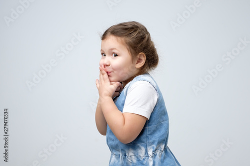 Surprised little girl covered mouth with her hands waiting for gift on her birthday being curious.