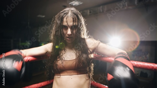 Young tired boxer woman standing on ring and resting. Sweat wet skin. Slow motion. © procinemastock