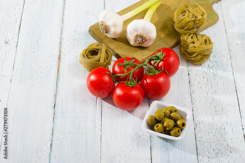 fresh tomato, garlic, olive, uncooked tagliatelle pasta on white wooden
