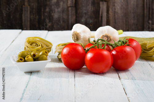 fresh tomato, garlic, olive, uncooked tagliatelle pasta on white wooden