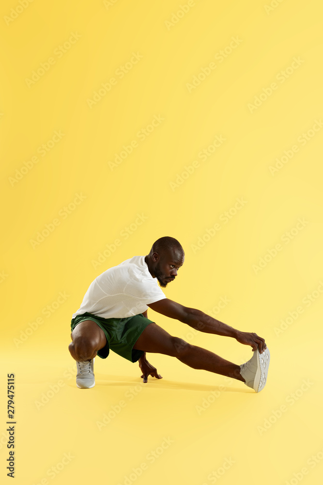 Man in sportswear stretching leg warming up on yellow background
