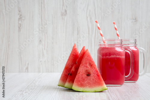 Skices of watermelon with smoothie in glass jars on a white wooden surface, side view. Copy space.