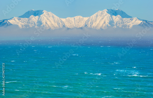 high mountain chain in a snow in a mist beyond emerald sea