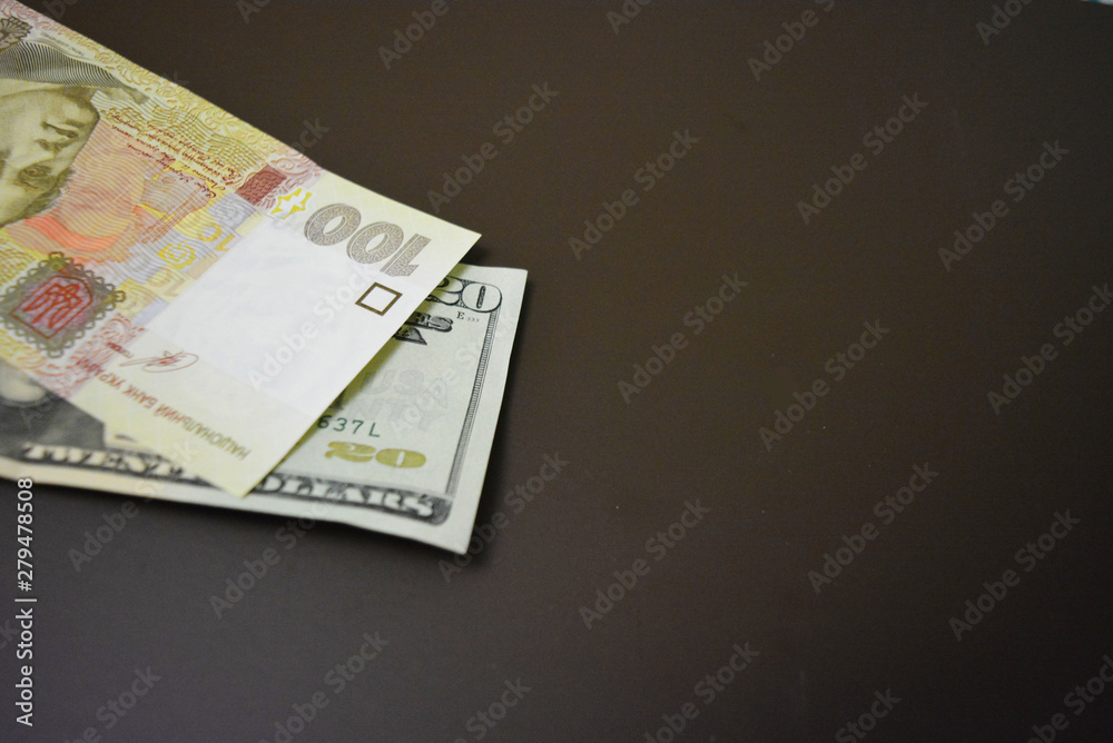 Paper bills in the size of USD 20 $ twenty American dollars and UAH 100 one hundred Ukrainian hryvnia on a brown matte background. Ukrainian and American currencies, payments and cash payments. Paper bills in the size of USD 20 $ twenty American dollars and UAH 100 one hundred Ukrainian hryvnia on a brown matte background. Ukrainian and American currencies, payments and cash payments.