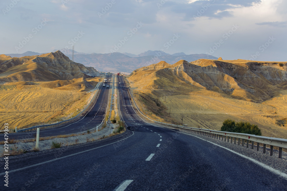 Highway of both directions in two lanes in each direction among the golden hills at sunset in desert