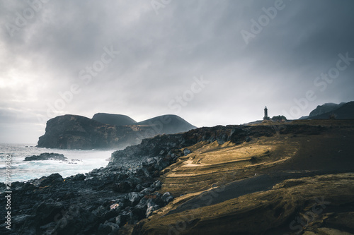 View over Capelinhos volcano, lighthouse of Ponta dos Capelinhos on western coast on Faial island, Azores, Portugal with a dramatic sunset and strong waves and clouds. Last volcano eruption was in